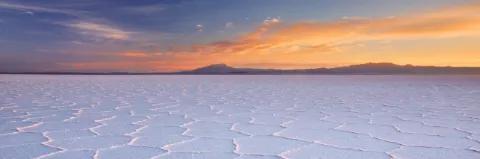 Der Himmel ist vom Sonnenuntergang rot gefärbt, darunter sind Berge. Davor ist ein Salzsee.