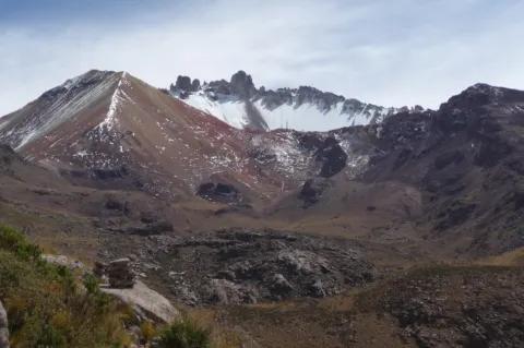 Im Hintergrund sind Berge. Einer dieser Berge ist in verschiedenen Rottönen gefärbt und teils schneebedeckt.