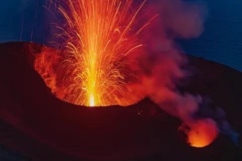 Es ist dunkel. Ein Vulkan bricht aus. Die Lava steigt in Funken nach oben.