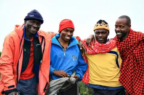 Vier afrikanische Männer stehen Arm in Arm nebeneinander und lächeln