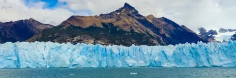 Perito-Moreno-Gletscher vor einem See und Bergkulisse im Hintergrund bei bewölktem Himmel
