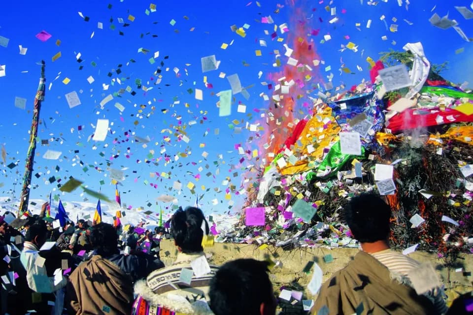 Eine Gruppe von Menschen schaut in Richtung Himmel. In der Luft fliegt buntes Papier und Farbe.