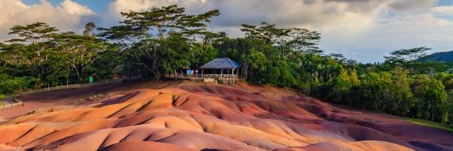 Sonne fällt auf Hügel mit vielen Brauntönen und grünen Bäumen und einer Hütte am Rand