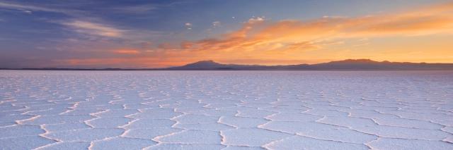 Der Himmel ist vom Sonnenuntergang rot gefärbt, darunter sind Berge. Davor ist ein Salzsee.