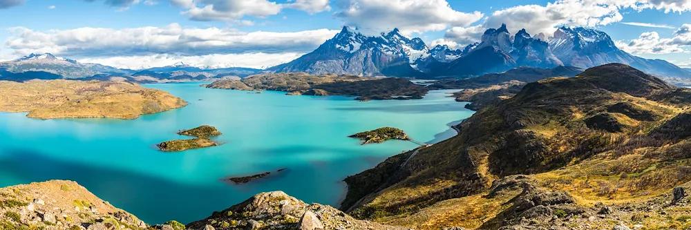 Ausblick auf grüne Berglandschaft, türkisblauen See mit Inseln und schneebedeckten Bergen