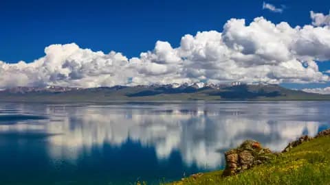 Ruhiger See mit Spiegelung der schneebedeckten Berge und Wolken.
