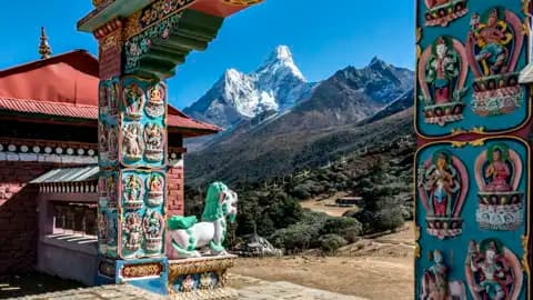 Blick durch ein kunstvoll verziertes Tor eines buddhistischen Tempels auf die schneebedeckten Himalaya-Gipfel.