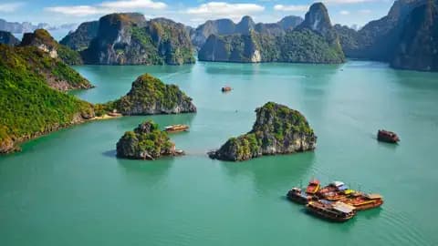 Panorama der Halong-Bucht mit bewaldeten Kalksteininseln und mehreren traditionellen Dschunken.