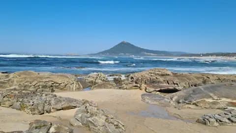 Felsiger Küstenabschnitt mit Blick auf einen Berg am Meer.