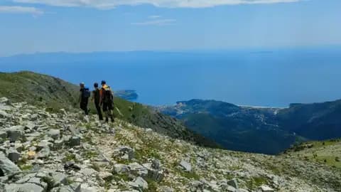 Wanderer auf einem Bergpfad mit Blick auf das Meer und eine Küstenstadt.