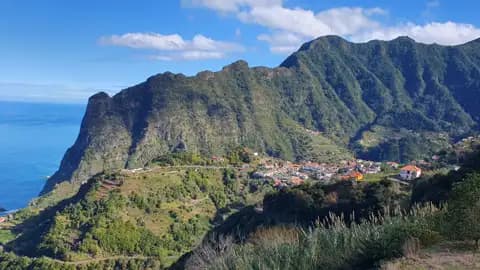 Panoramablick auf ein Dorf an der Küste, umgeben von grünen Bergen und dem Meer im Hintergrund.