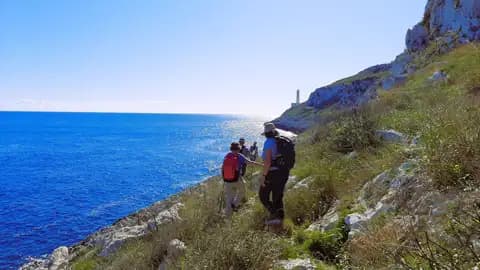 Wanderer auf einem Küstenpfad mit Blick auf das Meer und einen Leuchtturm in der Ferne.