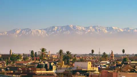 Blick auf die Dächer von Marrakesch mit dem schneebedeckten Atlasgebirge im Hintergrund.