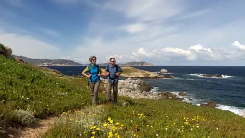 Zwei Wanderer auf einem blühenden Küstenpfad mit Blick auf das Meer.