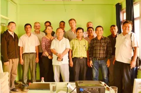 Eine internationale Gruppe von Menschen steht vor einer grünen Wand und blickt in die Kamera.