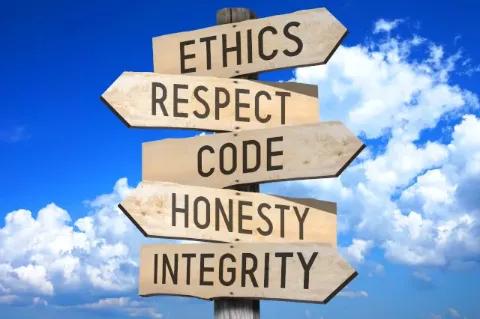 Vor blauem Himmel steht ein Wegweiser aus Holz. Die abgebildeten Begriffe lauten: Ethik, Respekt, Kodex, Ehrlichkeit und Integrität